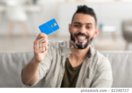 Happy young Arab man holding credit card, shopping from home, selective focus 82398727