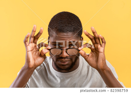 Poor eyesight. African american guy squinting eyes and looking at camera, touching eyeglasses over yellow background 82398759