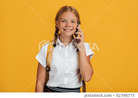 Cheerful smart european young girl student with pigtails and backpack talking on phone Cheerful smart european young girl student with pigtails and backpack talking on phone 82398775