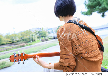 Short-haired woman playing acoustic guitar along the river 82398939