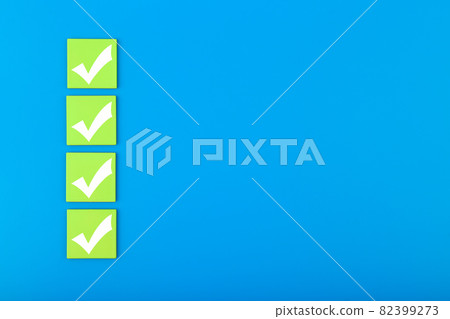 Four white checkmarks on green tablets in a row against blue background with copy space 82399273