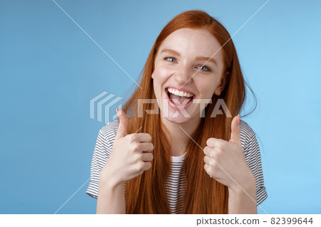 Enthusiastic amused outgoing redhead beautiful girl say yeah supportive like awesome idea show thumbs-up approval recommend gesture agree good choice, standing blue background 82399644