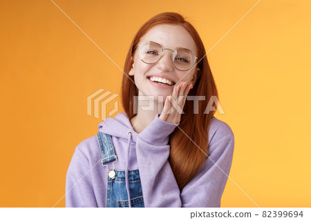 Charismatic happy tender redhead smiling european girl 20s glasses hoodie denim overalls having fun enjoying summer holidays chilly evening laughing joyfully touch pure clear skin, orange background 82399694