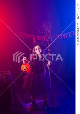 Little girl holds broom on Halloween holiday. Kid girl wear witch costume. Fantasy, fairy tale and masquerade concept. 82399727