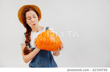 Young woman farmer is surprised by the size of the pumpkin harvest. 82399789