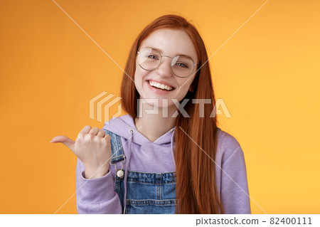 Cute helpful friendly-looking joyful european redhead woman show thumb left smiling delighted laughing pointing where find awesome store telling about interesting new promo offer, orange background Cute helpful friendly-looking joyful european redhead woman show thumb left smiling delighted laughing pointing where find awesome store telling about interesting new promo offer, orange background 82400111