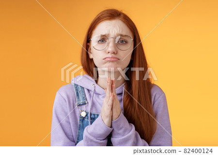Please beg you. Clingy upset sad caucasian redhead girlfriend wearing glasses frowning grimacing pouting pleading help asking favour need urgently borrow something, orange background 82400124
