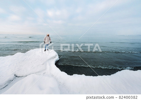 A tourist stands on the shore of the Baltic sea in winter. Winter near the Baltic States of Tallinn.Traveler near the sea in winter 82400382