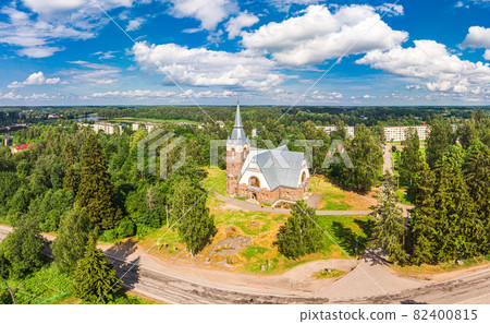 Aerial panoramic view to old lutheran church kirk Ryaysyalya designed by architect Joseph Stenback in style of Finnish romanticism, Art Nouveau in sunny summer day. Melnikovo, Leningrad region, Russia 82400815