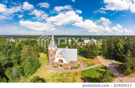 Aerial panoramic view to old lutheran church kirk Ryaysyalya designed by architect Joseph Stenback in style of Finnish romanticism, Art Nouveau in sunny summer day. Melnikovo, Leningrad region, Russia 82400817