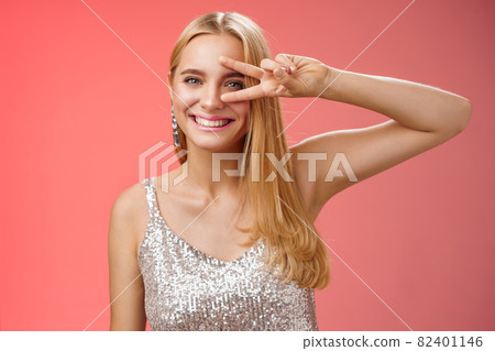 Joyful carefree attractive confident blond woman in stylish silver dress show disco sign victory peace gesture near eye smiling having fun enjoying awesome party grinning dancing red background Joyful carefree attractive confident blond woman in stylish silver dress show disco sign victory peace gesture near eye smiling having fun enjoying awesome party grinning dancing red background 82401146