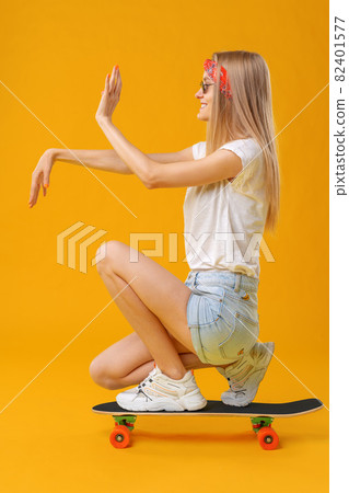 Pretty happy woman casually dressed sits on her skateboard 82401577