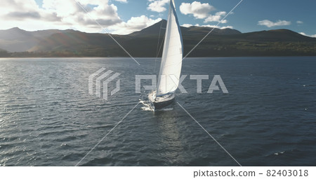 Luxury yacht race at sun light aerial. Yachting on serene seascape at open sea. Boat with white sail Luxury yacht race at sun light aerial. Yachting on serene seascape at open sea. Boat with white sail 82403018