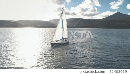 Slow motion yacht racing at ocean bay with highlang island coast aerial. Sun reflect at sailboat Slow motion yacht racing at ocean bay with highlang island coast aerial. Sun reflect at sailboat 82403019