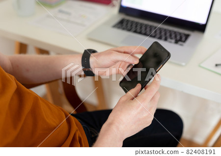 Closeup of hands holding smartphone and laptop in background 82408191