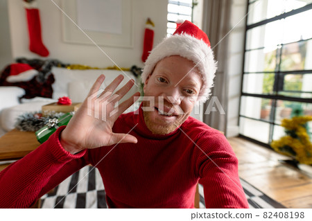 Albino african american man wearing santa hat making video call with christmas decorations 82408198