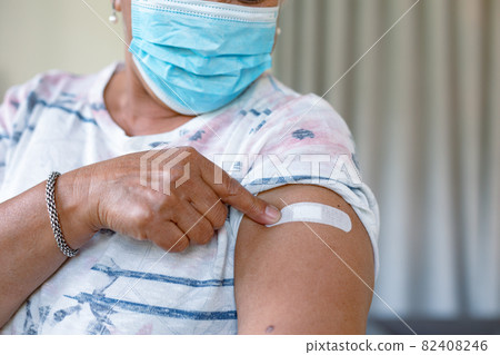 Senior mixed race woman in face mask showing plaster after vaccination Senior mixed race woman in face mask showing plaster after vaccination 82408246