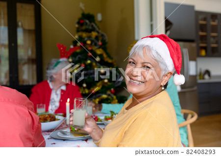 Happy mixed race senior woman holding glass and celebrating christmas with diverse group of friends Happy mixed race senior woman holding glass and celebrating christmas with diverse group of friends 82408293