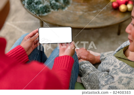Two diverse female friends using smartphone with copy space at christmas time 82408383