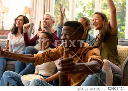 Group of happy diverse female and male friends watching tv and drinking beer together at home Group of happy diverse female and male friends watching tv and drinking beer together at home 82408421