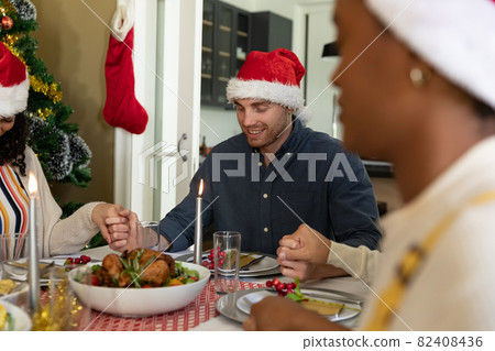 Caucasian man praying with friends at christmas table at home Caucasian man praying with friends at christmas table at home 82408436