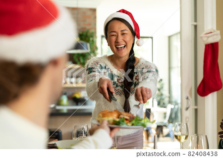 Happy asian woman in santa hat celebrating christmas with friends at home 82408438