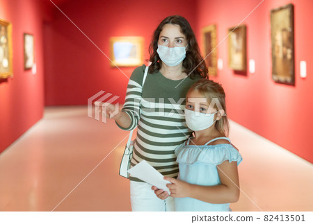Girl with woman in masks looking with interest at painting 82413501