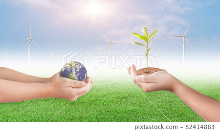 Hand holding young plant and earth globe on wind turbine with blue sky background. 82414883