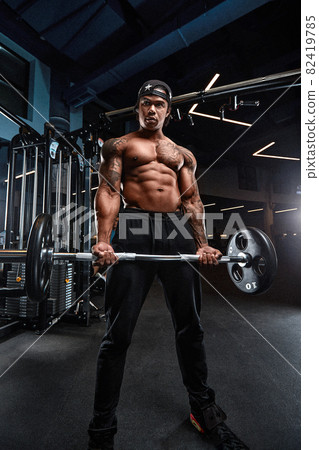 Strong and muscular afro-american man trains on modern equipment in gym. Portrait of muscular pumped up fitness trainer Strong and muscular afro-american man trains on modern equipment in gym. Portrait of muscular pumped up fitness trainer 82419785