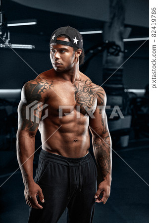 Strong and muscular afro-american man trains on modern equipment in gym. Portrait of muscular pumped up fitness trainer Strong and muscular afro-american man trains on modern equipment in gym. Portrait of muscular pumped up fitness trainer 82419786