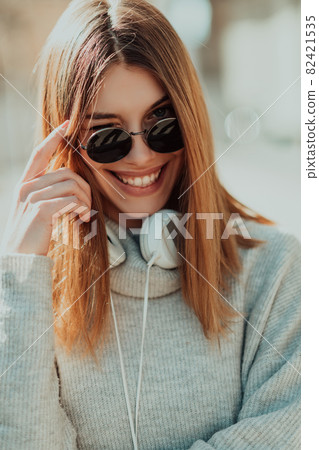 a modern girl with sunglasses walking down the street listens to music in headphones. a modern girl with sunglasses walking down the street listens to music in headphones. 82421535