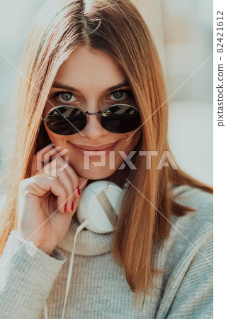 a modern girl with sunglasses walking down the street listens to music in headphones. 82421612