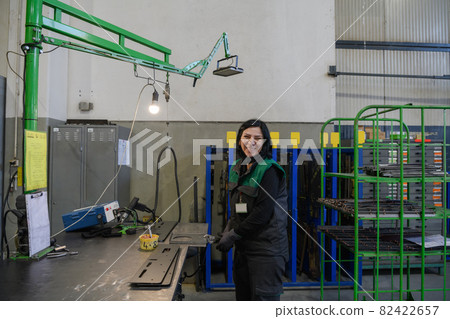 a portrait of a woman in uniform carrying a piece of metal and preparing it for the final part of production a portrait of a woman in uniform carrying a piece of metal and preparing it for the final part of production 82422657