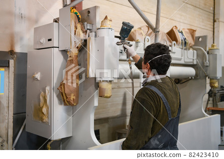 A worker painting to mechanical part with airless spray 82423410
