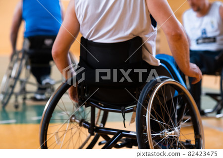Close up photo of wheelchairs and handicapped war veterans playing basketball on the court 82423475