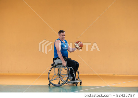 a war invalid in a wheelchair trains with a ball at a basketball club in training with professional sports equipment for the disabled. the concept of sport for people with disabilities 82423787