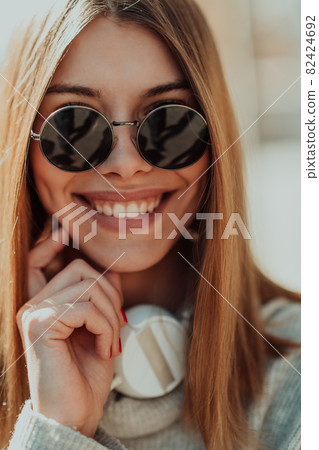 a modern girl with sunglasses walking down the street listens to music in headphones. a modern girl with sunglasses walking down the street listens to music in headphones. 82424692