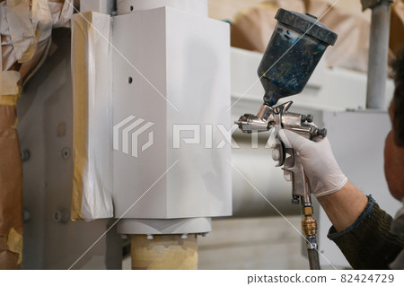 A worker painting to mechanical part with airless spray 82424729