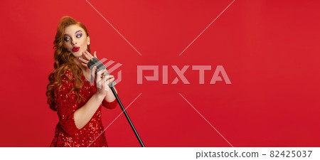 Cropped portrait of enthusiastic female jazz singer on stage isolated over red background. Flyer 82425037