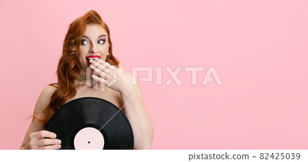 Portrait of beautiful excited Caucasian woman, singer holding vinyl record isolated over pink background. Flyer 82425039