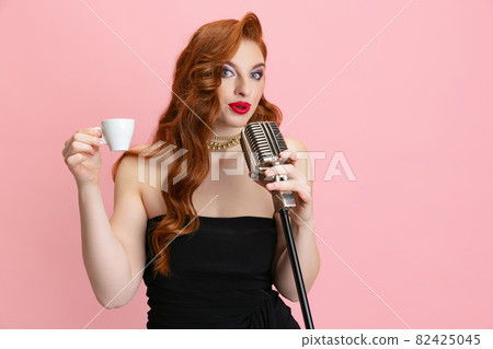 Cropped portrait of stylish Caucasian woman singing in microphone and holding espresso cup isolated over pink background Cropped portrait of stylish Caucasian woman singing in microphone and holding espresso cup isolated over pink background 82425045