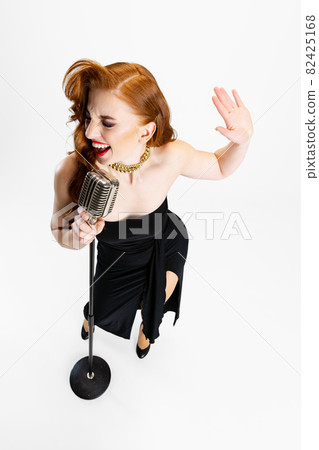 Top view full-length portrait of beautiful red-haired woman singing in microphone isolated over white background Top view full-length portrait of beautiful red-haired woman singing in microphone isolated over white background 82425168