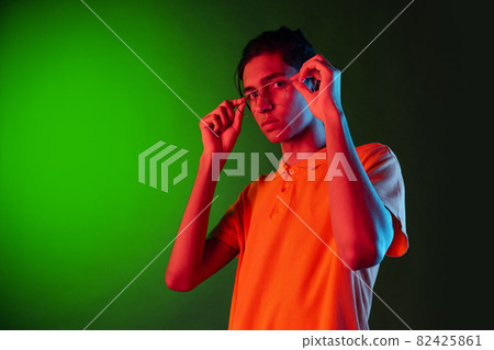 Close-up portrait of young man, student posing isolated on green studio backgroud in neon light. Human emotions concept. 82425861
