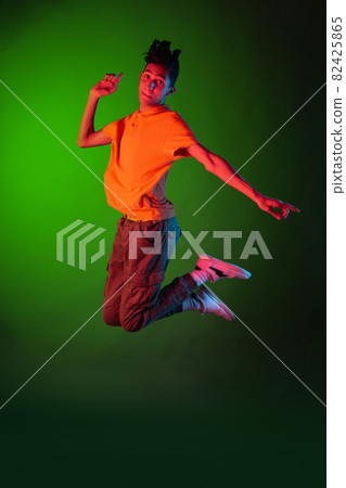 Portrait of young man, student in casual clothes jumping isolated on green vintage studio backgroud. Human emotions concept. 82425865