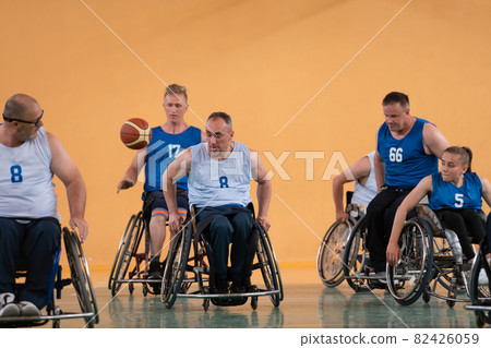 Disabled War veterans mixed race opposing basketball teams in wheelchairs photographed in action while playing an important match in a modern hall.  82426059