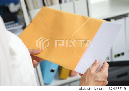 Businesswoman takes out documents from yellow envelope Businesswoman takes out documents from yellow envelope 82427749