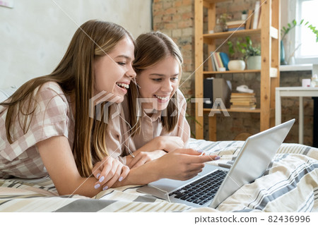 Two cheerful teenage girls discussing moment of online movie 82436996