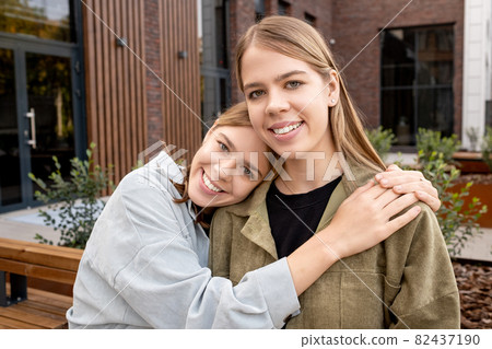 Affectionate twin girls in t-shirts and jackets looking at camera 82437190