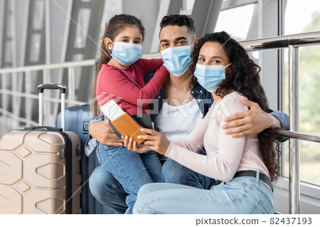 Young Arab Family Of Three Wearing Face Masks Waiting At Airport Terminal 82437193