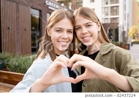 Happy affectionate twin girls making shape of heart with hands Happy affectionate twin girls making shape of heart with hands 82437224